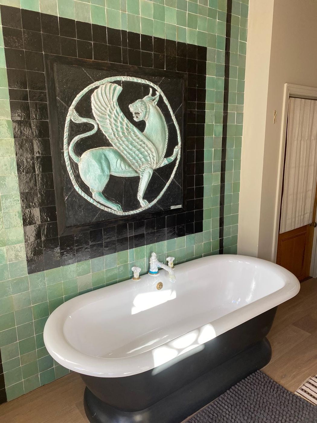White freestanding bath in front of a green tiled wall