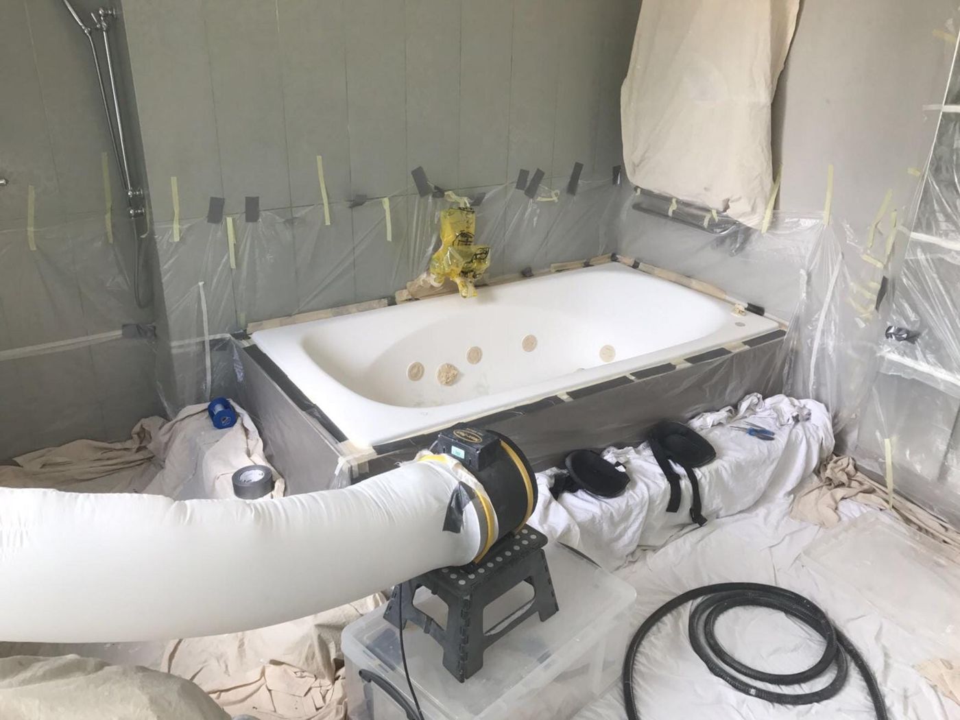 A bath masked up with dust sheets and an extraction hose before it is sprayed