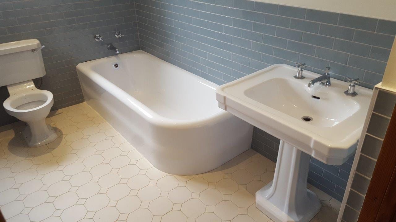 Restored bath and pedestal basin in a grey tiled bathroom