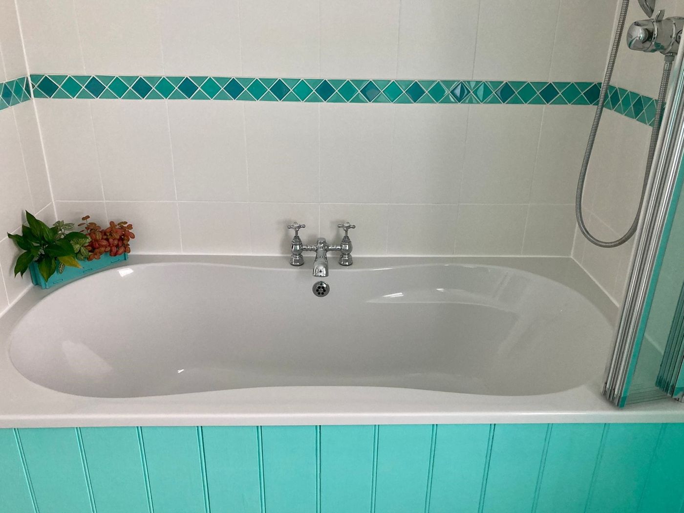 Restored white bath with a teal panelled side and tiled surround
