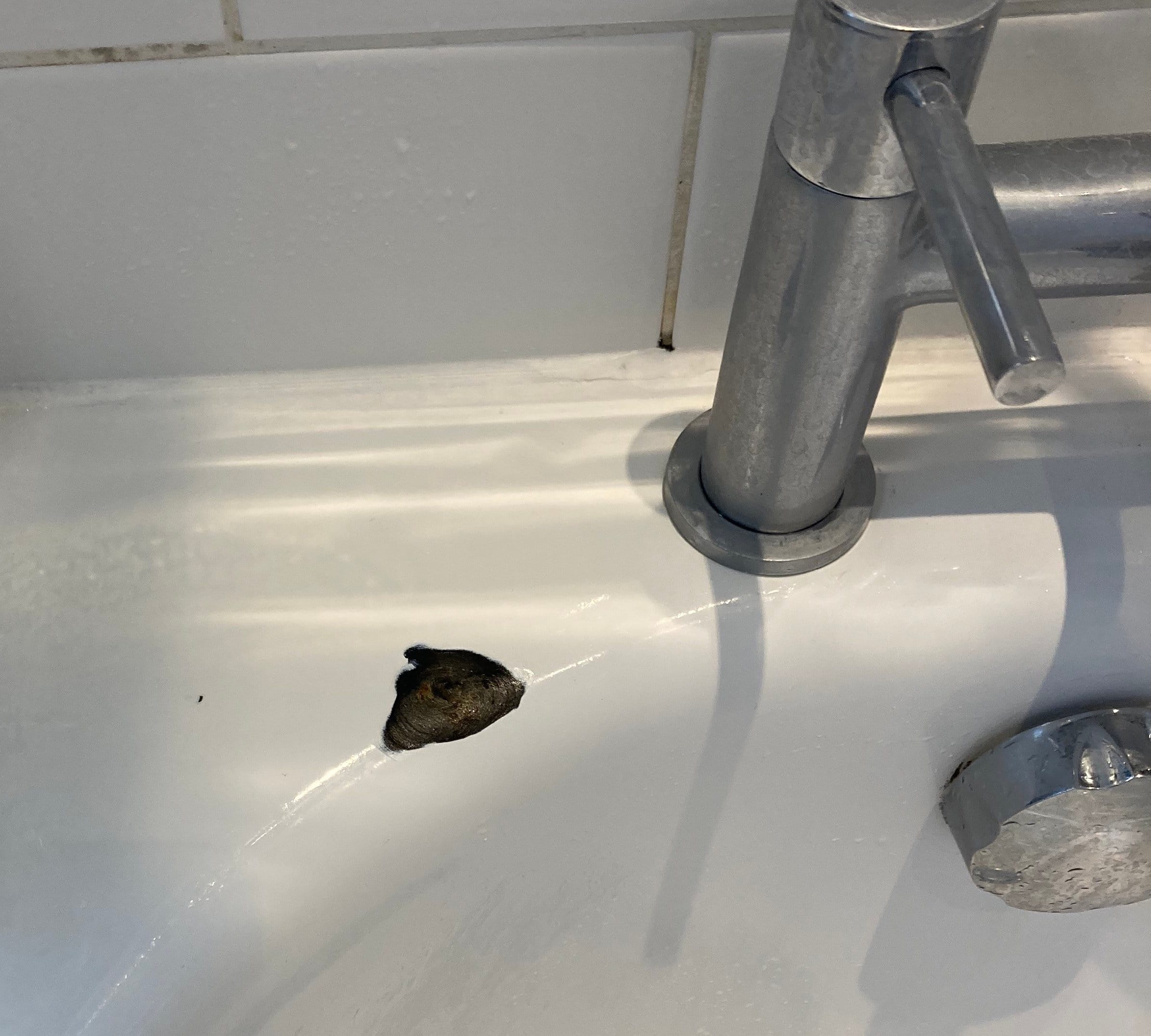 Basin with a dark chip beside the tap before repair