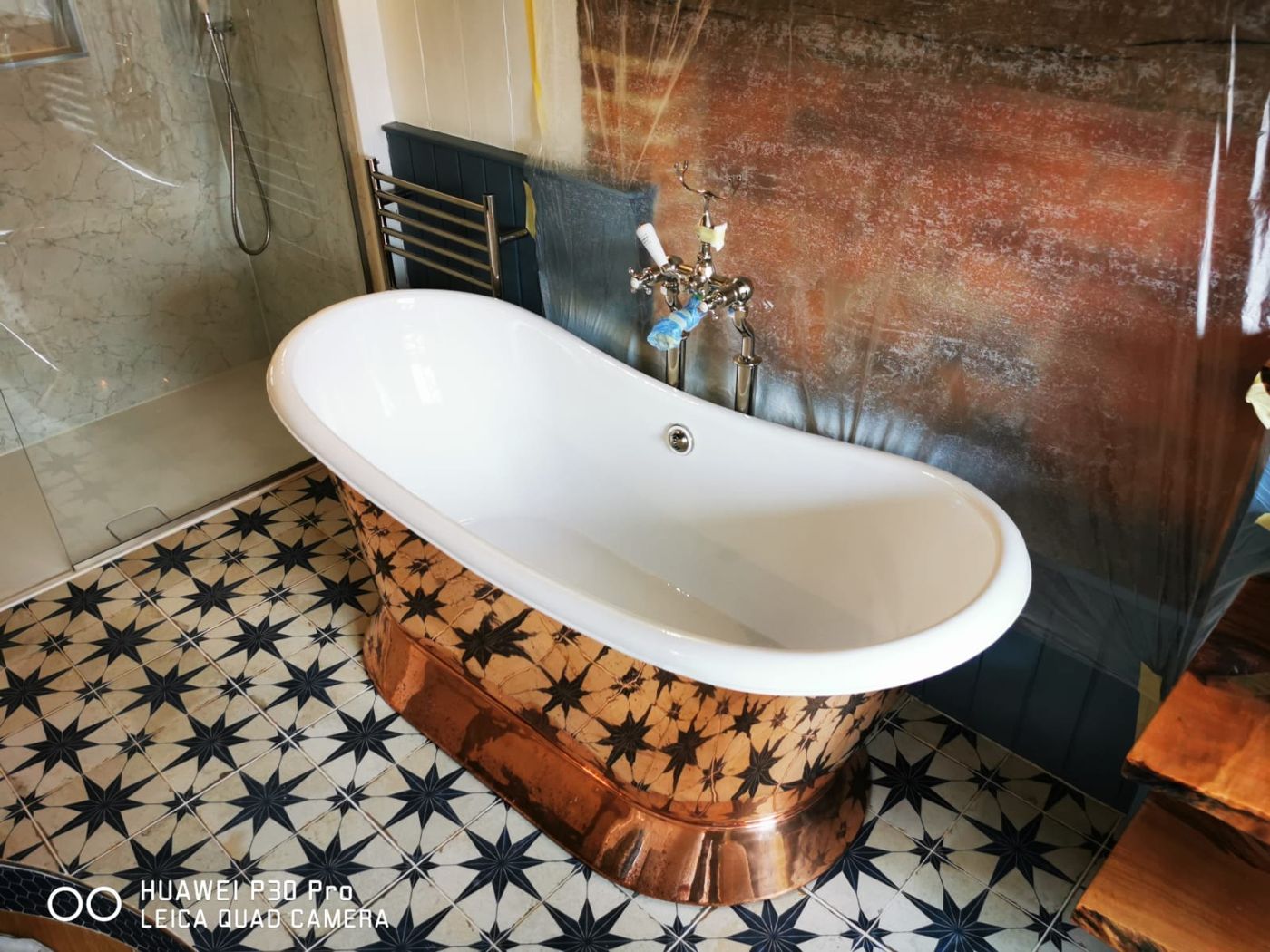 Freestanding bath with a copper-clad exterior on a star-patterned tile floor