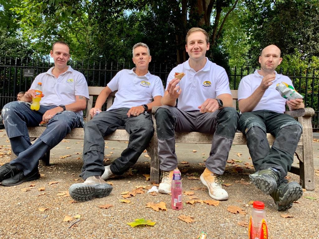 Four Mendabath technicians in company polo shirts sitting on a bench outdoors